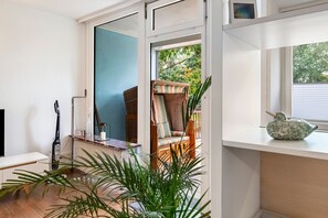 A room with a large window, a wicker chair, a small table, and a plant. - Studio 'AhoiPause Steinhude' with Lake View, Terrace and Beach Chair (Wunstorf)