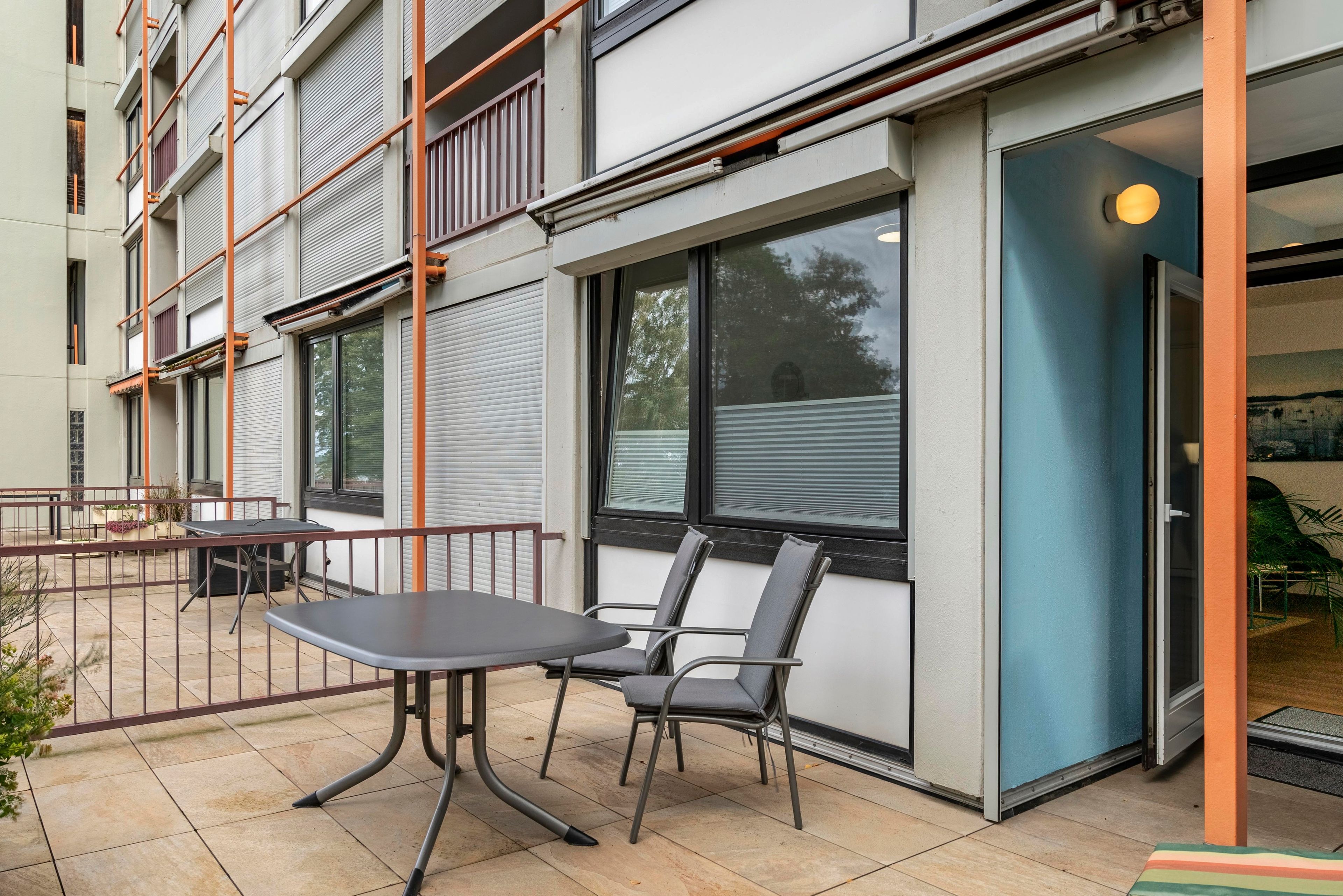 A building with a covered outdoor seating area, a door, and windows.
