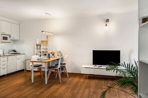 Una cocina moderna con armarios blancos, una mesa de comedor con sillas, una cafetera y un televisor de pantalla plana montado en la pared.