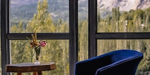 A room with a large window, a blue chair, and a small table with a vase of flowers.