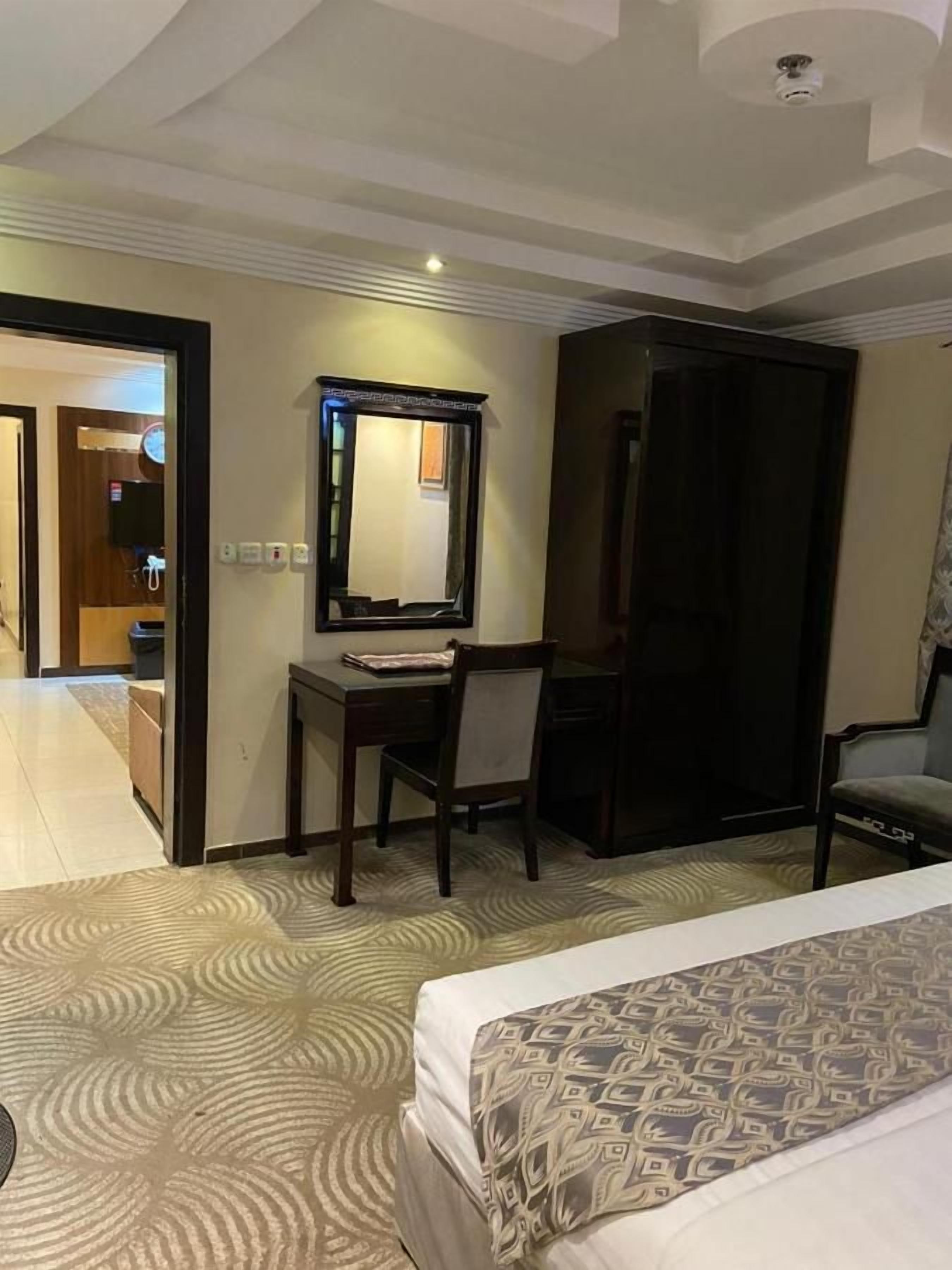 A hotel room with a bed, a desk with a chair, a mirror, and a wardrobe.