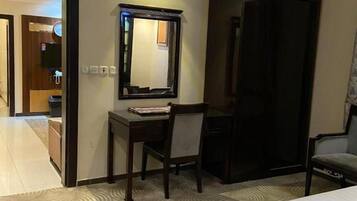 A hotel room with a bed, a desk with a chair, a mirror, and a wardrobe.