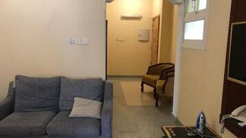 A living room with a sofa, a small table with an iron, a telephone, and a door leading to another room.