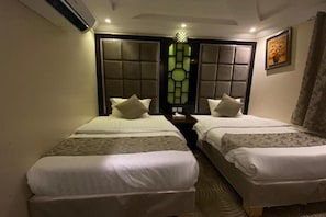 A hotel room with two beds, a window with a geometric pattern, and a framed picture on the wall.