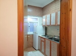 A compact kitchen with a refrigerator, a sink, and wooden cabinets.