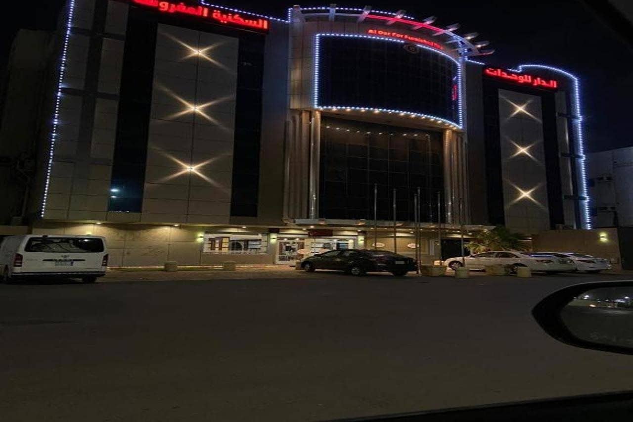 Un hôtel doté d’une façade moderne, d’une enseigne lumineuse et d’un parking où sont stationnés plusieurs véhicules.