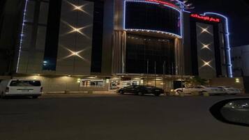 Un hôtel doté d’une façade moderne, d’une enseigne lumineuse et d’un parking où sont stationnés plusieurs véhicules.
