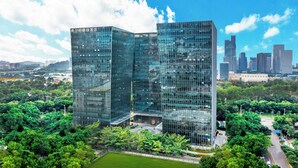 Un edificio moderno in vetro dal design angolare unico, circondato da alberi verdi e un cielo azzurro intenso.