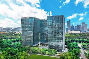 A modern glass building with a unique angular design, surrounded by lush green trees and a clear blue sky. - Home2 Suites by Hilton Shenzhen Nanshan Science & Technology Park (Shenzhen)