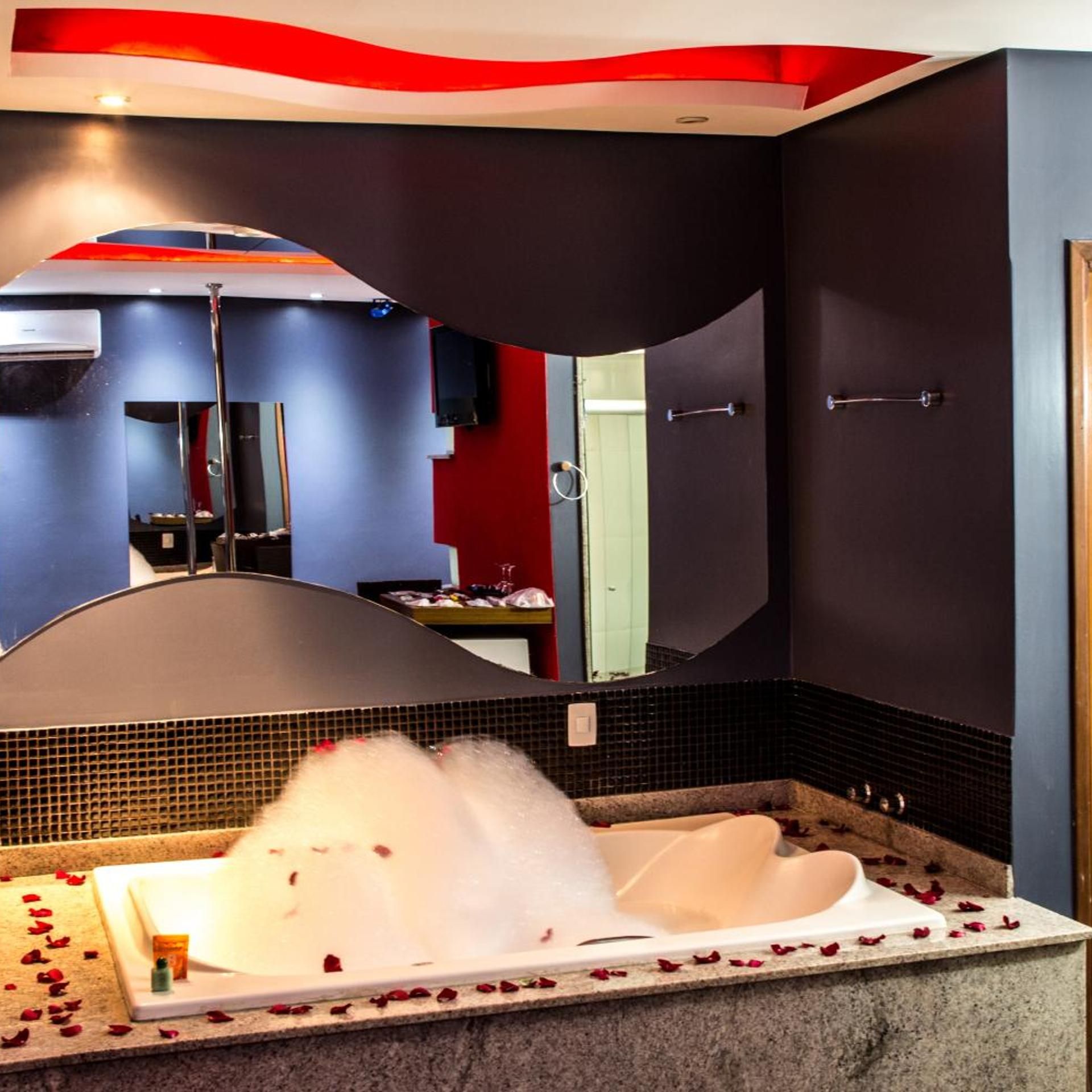 Um quarto de spa com banheira, espelho e decoração de parede em vermelho e preto.