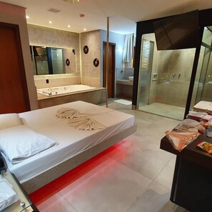 A modern hotel room with a large bed, a separate bathroom, and a glass-enclosed shower area. - Miragem Motel (Rio Verde)