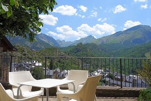 Un balcón con mobiliario de mimbre que da a un paisaje montañoso con un pueblo abajo.