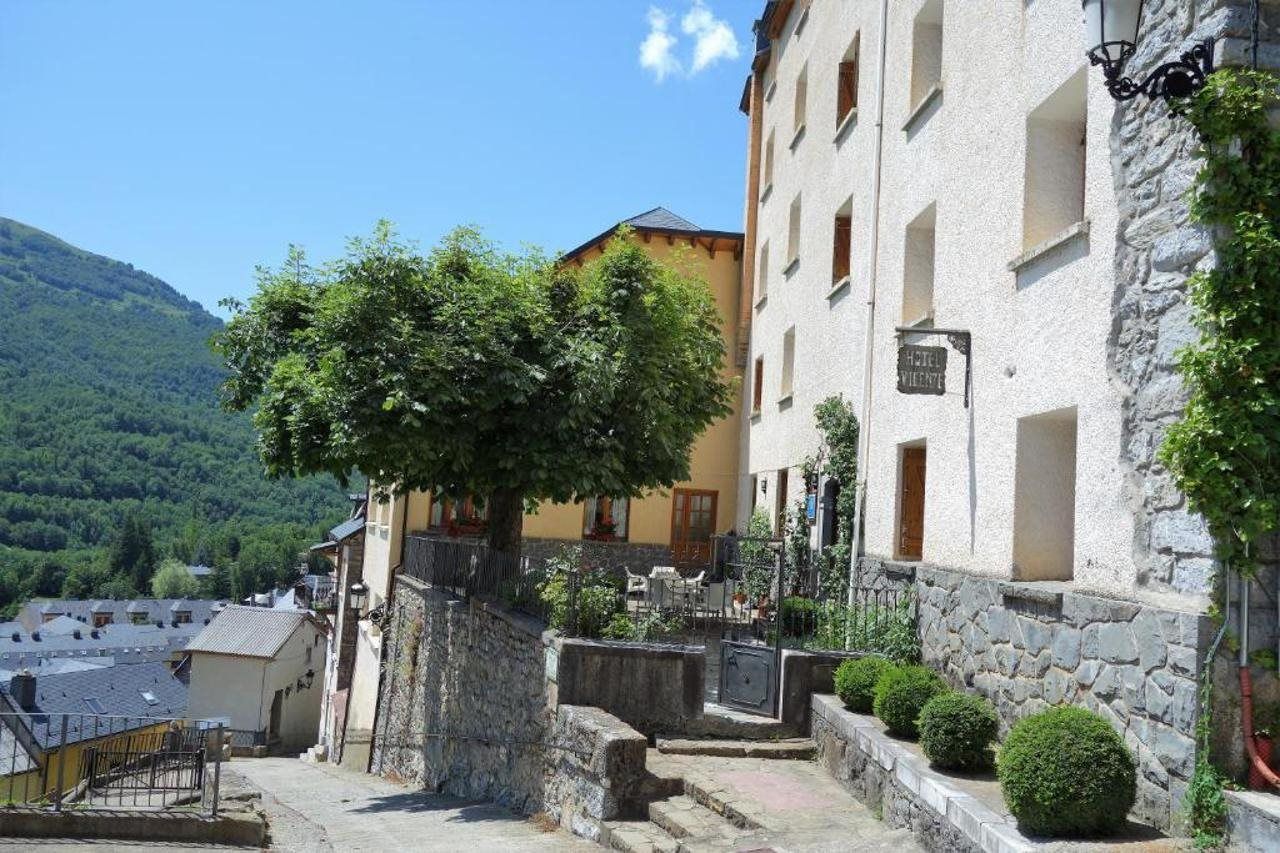 Un hotel con fachada de piedra, un árbol en primer plano y una montaña al fondo.