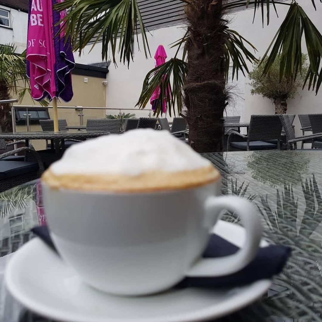 Una taza de café sobre una mesa, con vista a una terraza al aire libre y sombrillas.