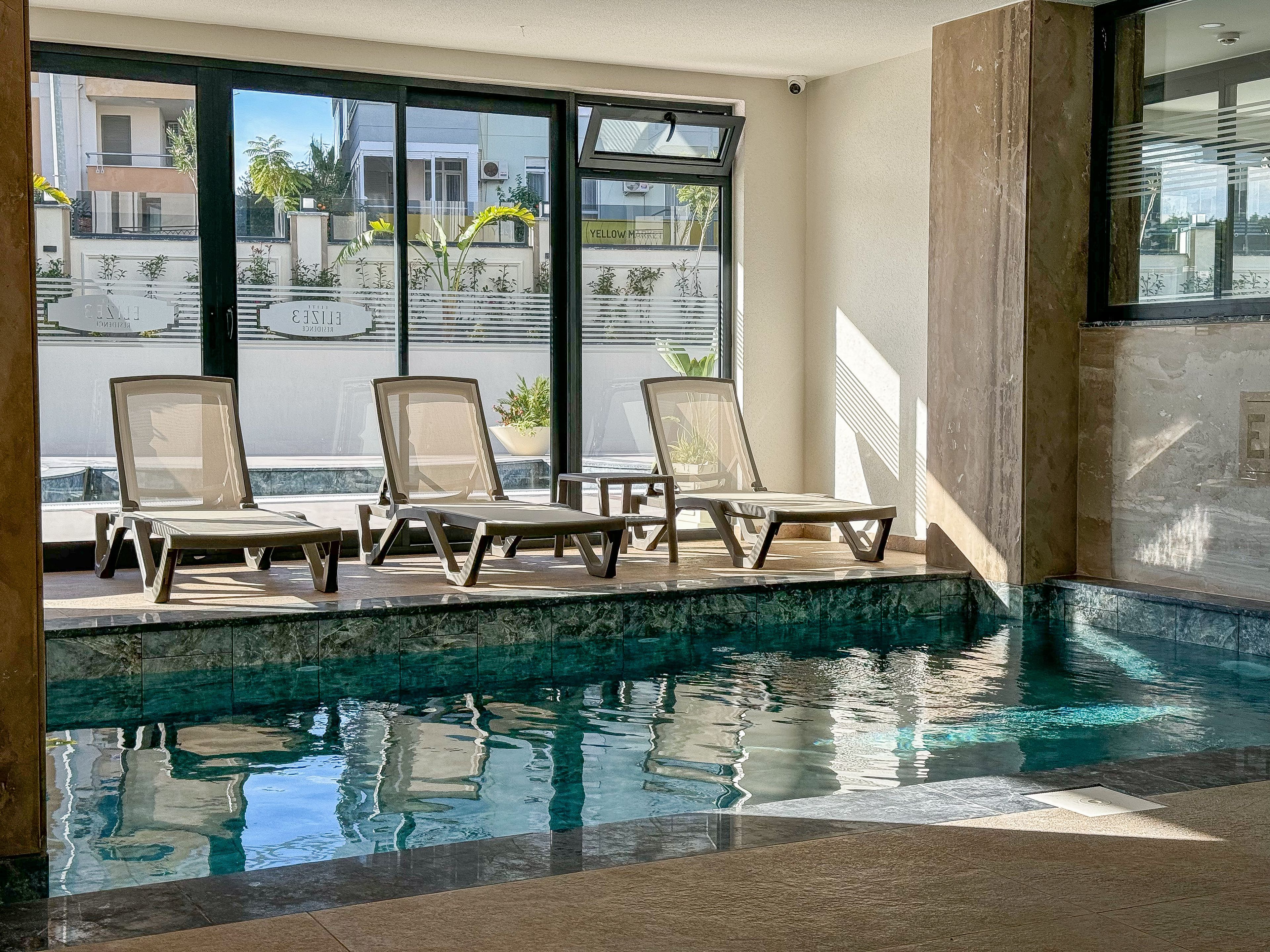 Ein Poolbereich mit Liegestühlen, freiem Ausblick ins Freie und einem gefliesten Boden.