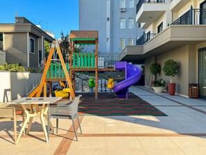 An outdoor play area with a slide, swings, and a table with chairs.