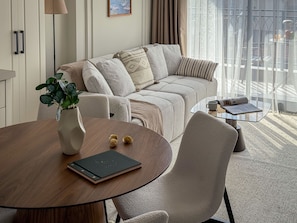 A modern living room with a sofa, a glass coffee table, a dining table, and a plant.