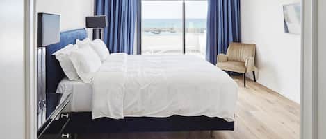 A hotel room with a bed, a TV, a chair, and a view of the sea.