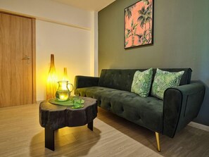 A room with a dark green sofa, a wooden door, and a wall with a tropical plant painting. - The Tree Skiathos (Skiathos)