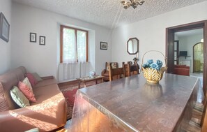 Ein Wohnzimmer mit einem Holzespeisetisch, einer Couch, einem Sessel und einem Fenster mit Spitzenvorhängen.