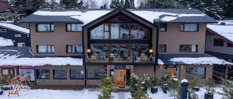 A multi-story building with a prominent balcony area, surrounded by snow-covered trees and a clear sky.