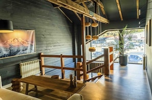 A wooden interior with a staircase, a table, and a view of the outside. - El Refugio Knapp (San Carlos de Bariloche)