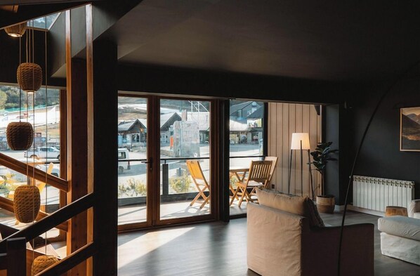 Een moderne woonkamer met een grote schuifpui die uitkomt op een balkon, een bank, een tafel en een vloerlamp.