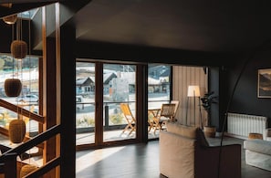 A modern living room with a large sliding glass door leading to a balcony, a sofa, a table, and a floor lamp. - El Refugio Knapp (San Carlos de Bariloche)