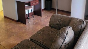 A living room with a sofa, a small desk with a chair, and a trash can. - Mumo Resort (Badplaas)