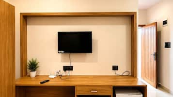 Un espacio habitable moderno con un televisor de pantalla plana montado en un mueble de madera, un refrigerador pequeño y una planta en maceta.