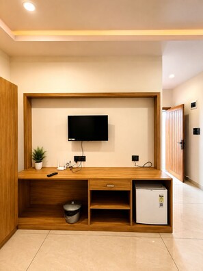 A modern living space with a flat-screen TV mounted on a wooden wall unit, a small refrigerator, and a potted plant.
