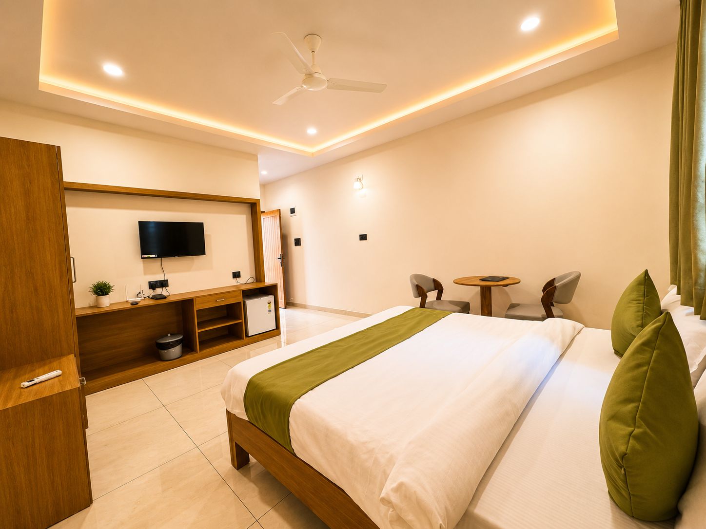 A hotel room with a bed, a desk with a TV, a ceiling fan, and a small table with chairs.