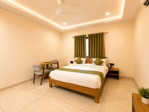 A hotel room with a bed, a small table, two chairs, a ceiling fan, and a potted plant. - StayGuru Palm Glow Resort (Bhuj)