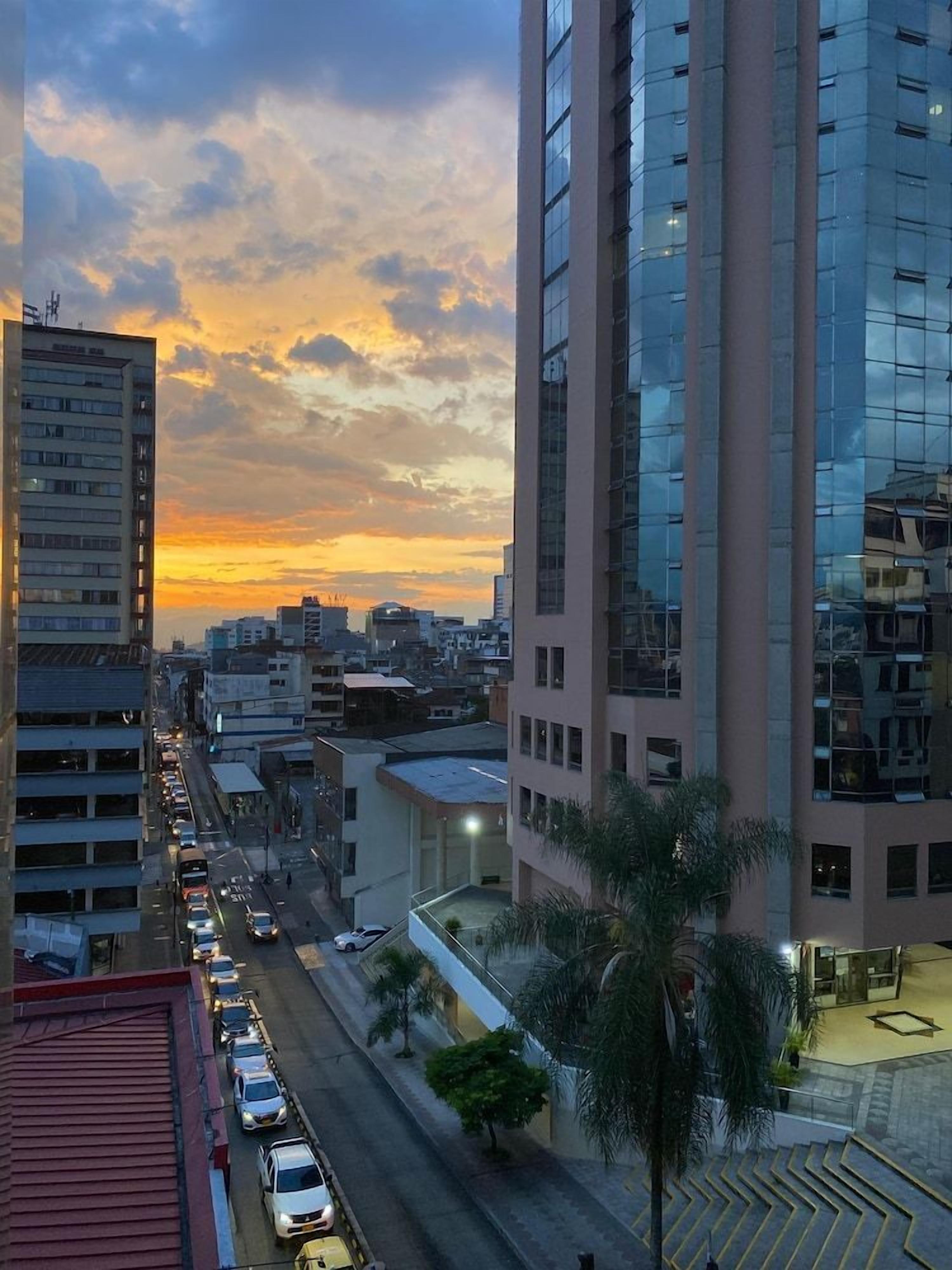 A cityscape with tall buildings, a busy street, and a sunset.