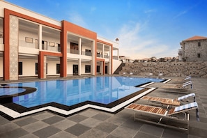 A swimming pool with lounge chairs and a building with balconies. - Bookmark Resort Jogi Mahal Ranthambore (Sawai Madhopur)