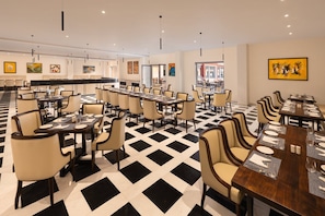 A hotel dining area with multiple tables and chairs, a checkered floor pattern, and artwork on the walls. - Bookmark Resort Jogi Mahal Ranthambore (Sawai Madhopur)