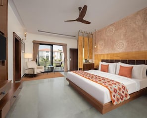 A hotel room with a large bed, a ceiling fan, a TV, a desk, and a balcony with a view. - Bookmark Resort Jogi Mahal Ranthambore (Sawai Madhopur)