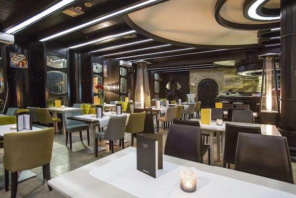 A modern restaurant interior with tables, chairs, and a central staircase. - Zepter Hotel Drina (Bajina Bašta)