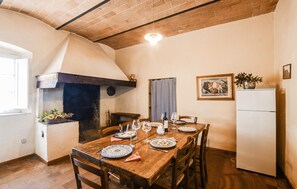 Ein Essbereich mit einem Holztisch, gedeckt für vier Personen, einem Backofen aus Ziegeln und einem weißen Kühlschrank.