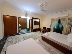 Une chambre d’hôtel avec deux lits, un coin salon avec une table et des chaises, une télévision et une armoire.