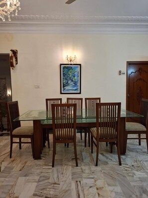 Un coin repas avec une table en verre entourée de chaises en bois, un tableau au mur et une porte portant un numéro.