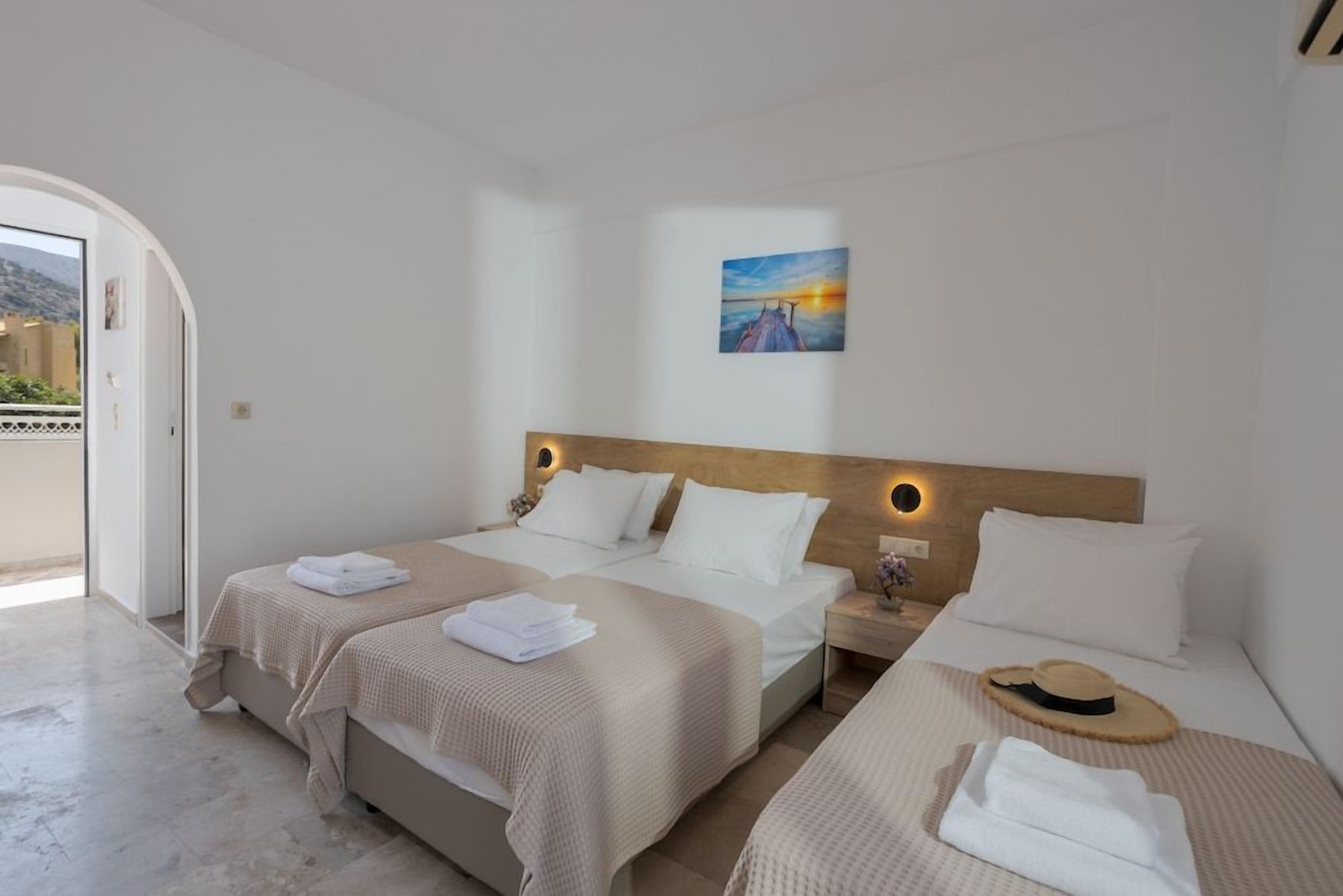 A hotel room with two beds, a painting on the wall, and a view through an open door.