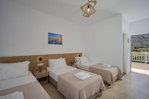 A hotel room with three beds, a painting, a wooden headboard, and a balcony with a view. - Amara Seaside (Hersonissos)