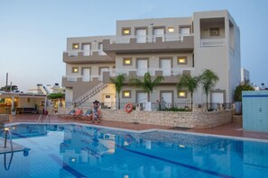 A multi-story hotel with a swimming pool, outdoor seating, and a stone wall with palm trees. - Amara Seaside (Hersonissos)