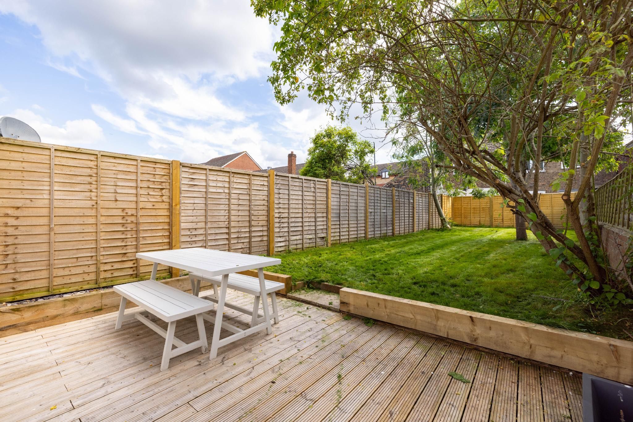 A wooden deck with a picnic table and benches, surrounded by a wooden fence and a well-maintained lawn.