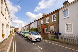 Una calle residencial con casas adosadas, coches aparcados y cielo despejado.