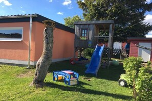 A playground with a slide and a small playhouse, a tree, and a building with a window. - Holiday home in Frauenwald with barbecue (Frauenwald)
