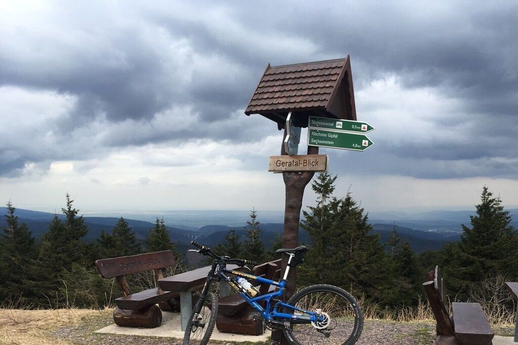 A mountain viewpoint with a directional signpost, a bicycle, and a bench.