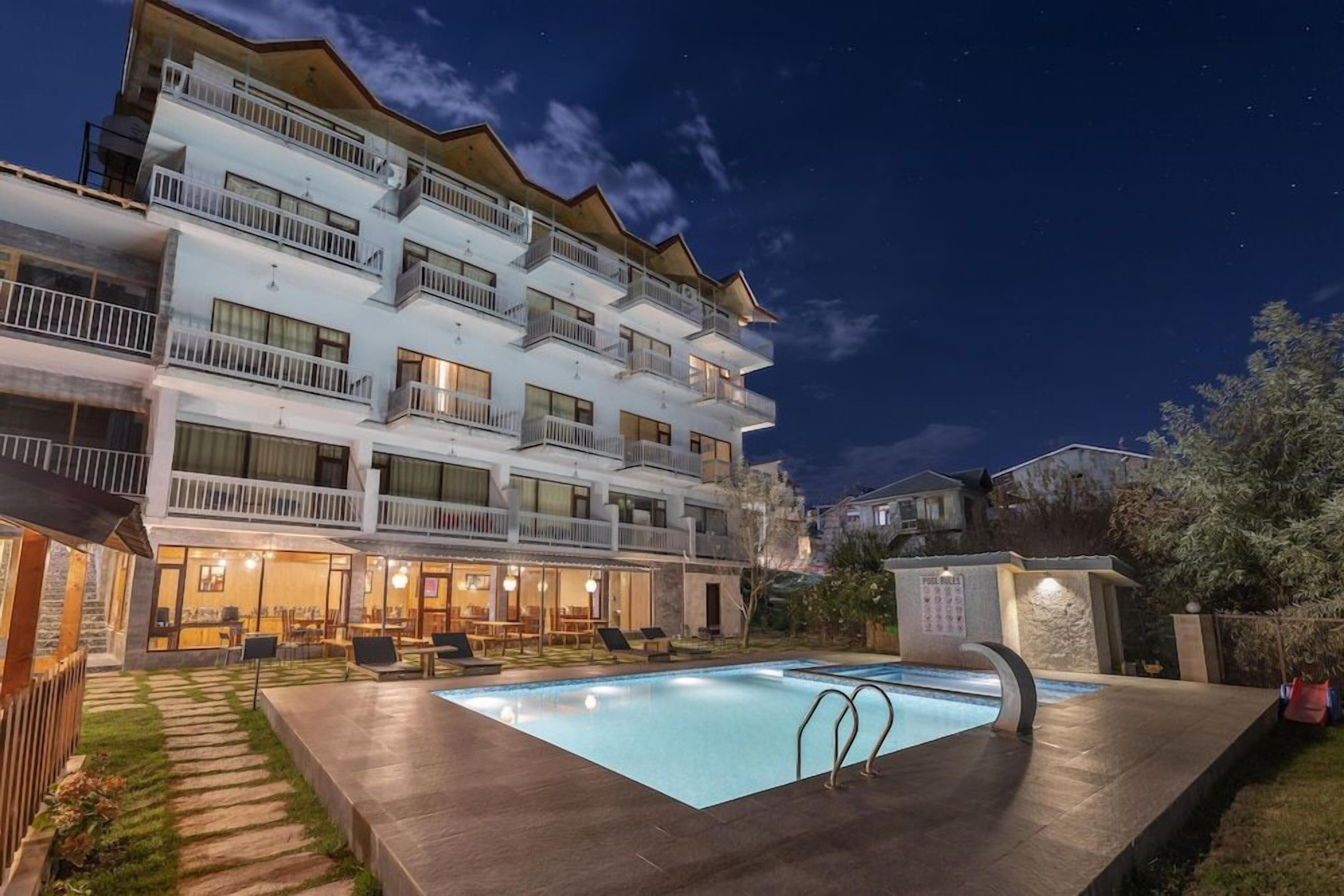 A multi-story hotel with a swimming pool, outdoor seating, and a well-lit balcony area.