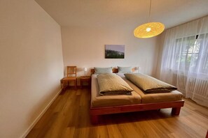 Ein Schlafzimmer mit einem hölzernen Bett, einem Nachttisch, einem Sessel und einer Pendelleuchte.